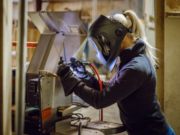 A welder performing a weld in a full face shield and gloves.